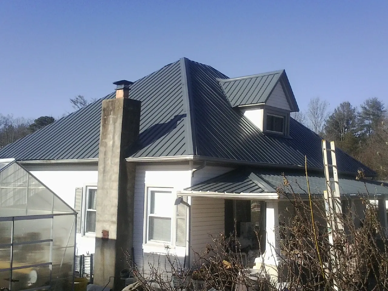 Dark blue standing seam metal roof on a white farmhouse with dormer — Slate & Tile Roof Repair by Roofing Brothers in Bonham