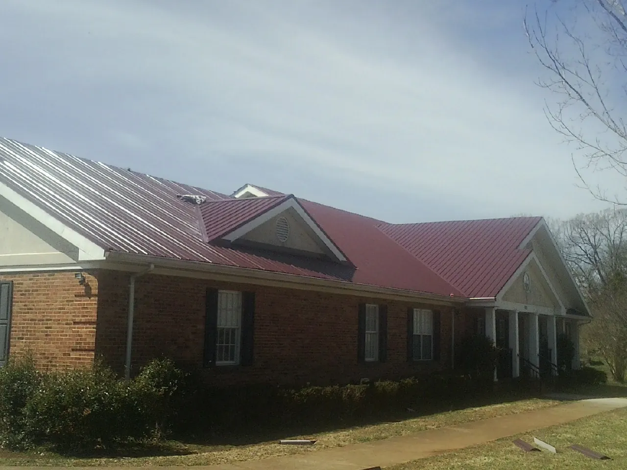 Red metal roof with gabled entries on a long brick building, from a Hail Damage Roof Repair job in Bonham