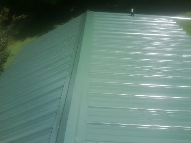 New green metal panels meeting at the ridge of a roof — Flat Roof Repair work by our crew in Bonham
