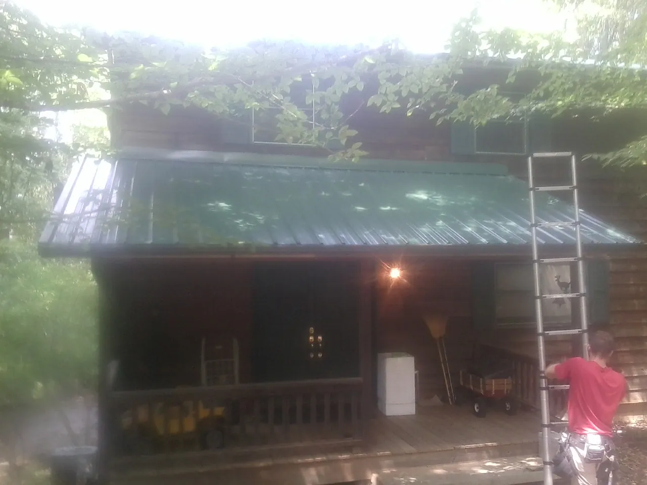 Worker on a ladder at the green porch roof of a wooded cabin in Bonham