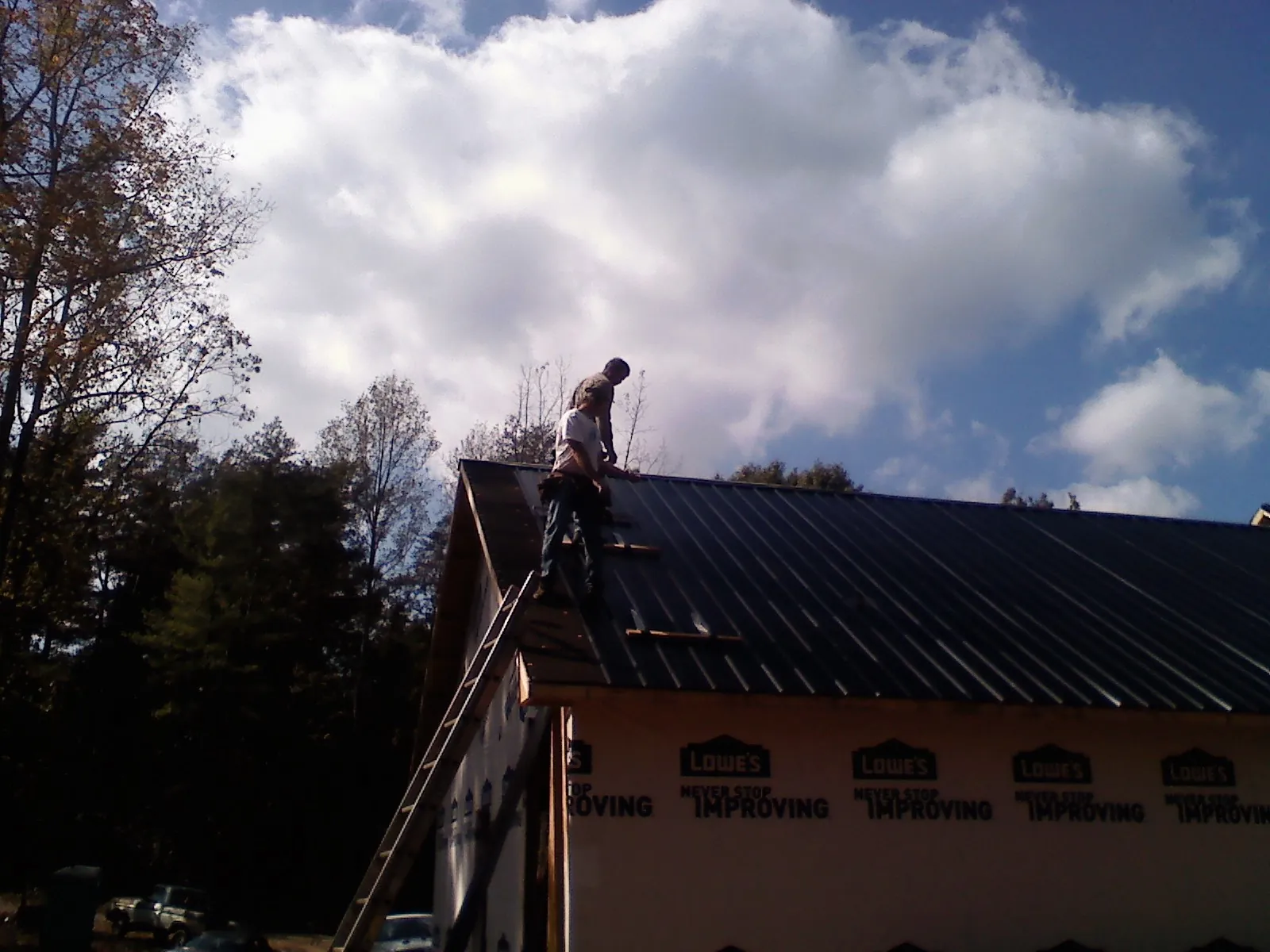 Roofer fastening dark metal panels high against a cloudy sky, from a Roof Inspection job in Bonham